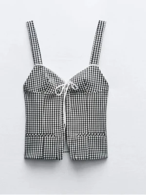 Rutig korsettopp från Zara  - Säljer en trendig korsettopp i svartvitt rutigt mönster. Toppen har breda axelband, dekorativ knytning framtill och en liten slits nedtill. Perfekt att styla med jeans eller kjol för en cool look.