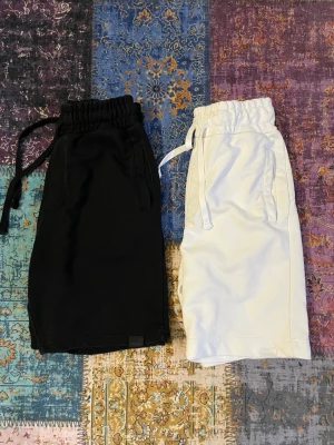 Svarta och vita shorts  - Två par shorts i svart och vitt med elastisk midja och dragsko. Modellen har raka ben och sidofickor, tillverkade i mjukt tyg som känns skönt mot huden. Perfekta för en avslappnad och trendig stil.