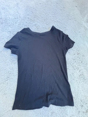 Svart basic t-shirt - En enkel svart t-shirt med rund hals och korta ärmar. Perfekt att matcha med jeans eller kjol för en clean och stilren look. Tillverkad i mjuk bomull för skön känsla hela dagen.