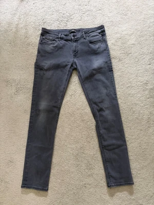 Grå slim fit jeans från Replay - Snygga grå slim fit jeans från Replay med fem fickor och diskreta slitningar. Jeansen har klassisk knappgylf och bälteshällor. Perfekta för dig som gillar en modern och stilren look. Pris kan diskuteras.