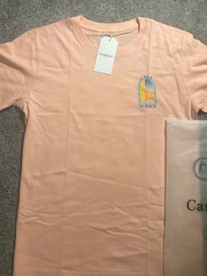 Ljusrosa t-shirt från Casablanca - Säljer en ljusrosa t-shirt från Casablanca med trycket 'Casa Blanca' och ett färgglatt motiv på bröstet. T-shirten har rund hals och korta ärmar. Tillverkad i mjuk bomull för en skön känsla.