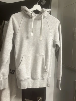 Russmerch hoodie  - En stilren ljusgrå hoodie med huva och snörning. Hoodien har en stor magficka framtill och ribbade muddar vid ärmslut och nederkant. Perfekt för en avslappnad och bekväm stil. Tröjan är i bra skick, Om ni är intresserade av hela sättet så kan ni höra av er också, så kan vi komma överens om något. 