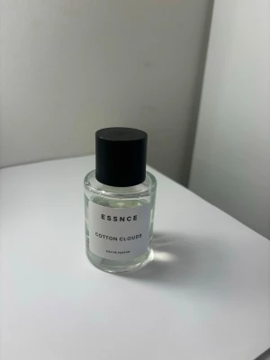 ESSNCE Cotton Clouds parfym - Fräsch parfym från ESSNCE med doften Cotton Clouds. Flaskan är cylindrisk i genomskinligt glas med svart lock och stilren vit etikett. Perfekt för dig som gillar lätta och rena dofter. Använd lite, doften passar inte mig personligen därav säljes 
