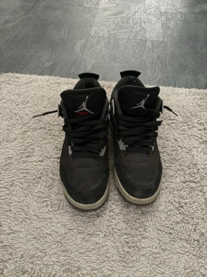 Svarta Air Jordan 4 sneakers - Säljer ett par svarta Air Jordan 4 sneakers med vita och grå detaljer samt Jumpman-logga på plösen. Skorna har en klassisk hög siluett, meshpaneler och robust sula. Perfekta för dig som gillar streetwear och vill ha en ikonisk look. Box ingår. 