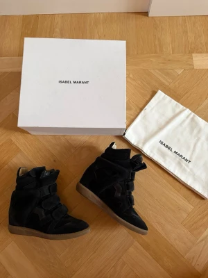 Isabel Marant skor  - Säljer ett par svarta höga sneakers från Isabel Marant i mocka och läder. Skorna är använda ett par fåtal gånger. De är i storlek 38 och i färgen svart. Nypris är 6500 kronor. Kartong och dustbag kommer med. 