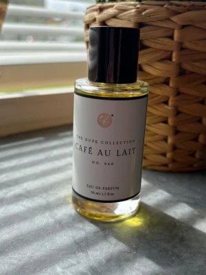 Café Au Lait Eau de Parfum 50 ml - Parfymflaska från The curiosa med doften Café Au Lait. Flaskan är cylindrisk i genomskinligt glas med svart plastlock och vit etikett. Innehållet är ljusgult och flaskan rymmer 50 ml. Elegant och stilren design som passar perfekt på parfymhyllan.