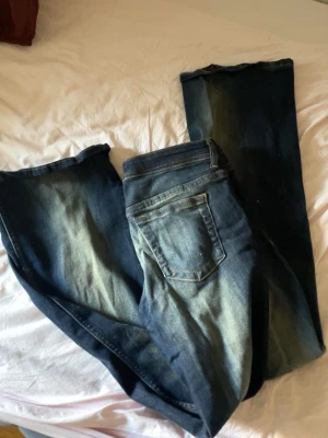 Mörkblå utsvängda jeans - Säljer ett par mörkblå jeans med snygga slitningar och tvättade detaljer. Klassisk femficksmodell med gylf och knapp. Jeansen har kontrastsömmar och är tillverkade i stretchigt denimtyg för en bekväm passform.