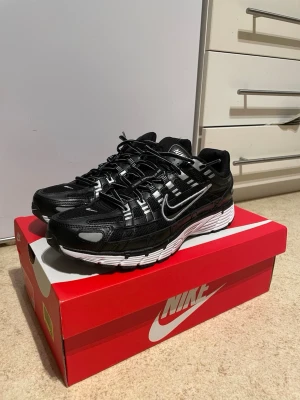 Nike P-6000 svart/vit sneakers - Nike P-6000 sneakers i svart och vitt med mesh och syntetiska överdrag. Skorna har en sportig design med tydliga detaljer, reflekterande inslag och en tjock vit sula. Swoosh-logga på sidan och P-6000-tryck på hälen. Perfekta för dig som gillar streetwear.