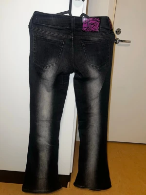 Svarta bootcut jeans med slitningar - Säljer ett par svarta/mörkgråa bootcut jeans med snygga tvättade detaljer längs benen. Jeansen har fem fickor och en lila patch bak i midjan. Nypris 399 kr!! Använd högst 5 ggr. Säljer pga att de är för små i midjan💗💗