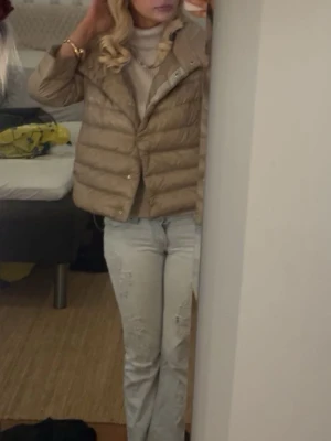 Beige pufferjacka från Herno - Snygg beige pufferjacka från Herno med kortare boxy passform och bred krage. Jackan har trekvartsärmar, tryckknappar framtill och är tillverkad i ett glansigt, lätt material som ger en lyxig känsla. Perfekt för kalla vinterdagar, och hösten 