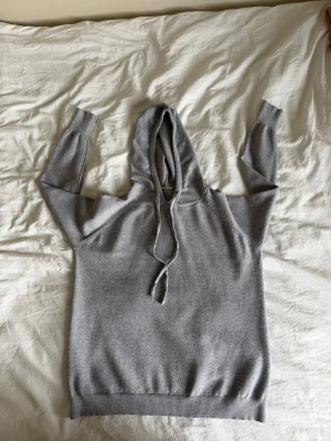 Ljusgrå Kashmir hoodie - Kashmir hoodie En stilren ljusgrå hoodie med luva och dragsko. Tillverkad i mjukt material, perfekt för en avslappnad look. Långa ärmar och ribbade muddar vid ärmslut och nederkant. Passar perfekt till jeans eller mjukisbyxor.