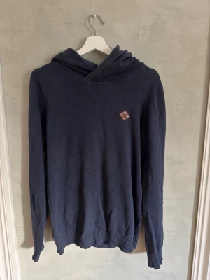 Mörkblå hoodie - Mysig marinblå hoodie från house basic med snygg överlappande design på huvan i fram  och en liten patch på bröstet. Perfekt för dig som gillar en enkel och stilren look. Skick 8/10, storlek M, Hör av dig vid frågor 🙌