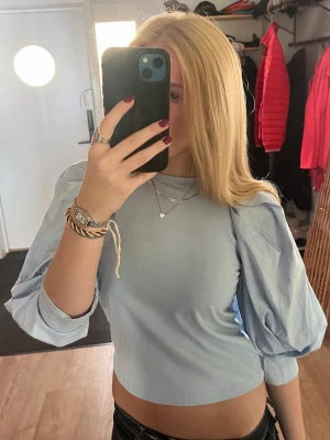 Ljusblå croppad topp med puffärm - Säljer en ljusblå croppad topp med puffiga trekvartsärmar. Toppen har en enkel och stilren design med rund halsringning och är tillverkad i ett mjukt bomullsliknande material💕