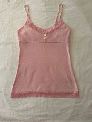 Rosa linnetopp med spetsdetaljer - Ljusrosa ribbad camisole med fina spetsdetaljer och en liten knappslå framtill vid halsringningen. Den liknar väldigt mycket Hollisters modeller. 💕Den har lite gul missfärgning sista bild
