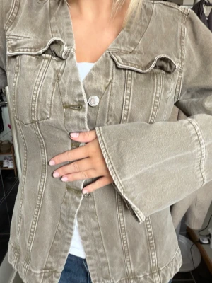 Beige jeansjacka med vida ärmar - Snygg beige jeansjacka med markerade sömmar och vida ärmar. Jackan har två bröstfickor med lock och knappar framtill. Passformen är något figursydd och materialet är klassiskt denim. Perfekt för dig som vill ha en unik twist på den klassiska jeansjackan.