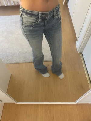 Bootcut ljusblå jeans med nitar - Säljer ett par ljusblå bootcut jeans med snygga silverfärgade nitar längs fickorna och benen,som inte har lossnat. Designen finns bara i Becca men är väldigt lågmidjade. Jeansen är helt nya och har bara använts 2 gånger.