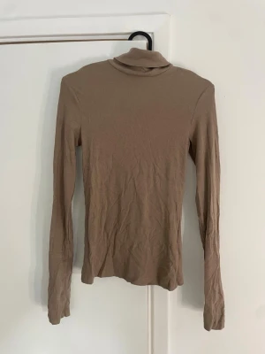 Beige polotröja från H&M - Slimmad beige polotröja från H&M i mjukt och stretchigt material. Tröjan har långa ärmar och en klassisk polokrage, perfekt att styla lager på lager. Enkel och stilren design som passar till det mesta.