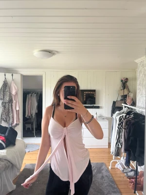 Ljusrosa knyt topp från Gina Tricot - Supersöt ljusrosa topp från Gina Tricot i mjukt material. Toppen har smala axelband, knyt framtill och en croppad passform. Perfekt för sommardagar och enkel att styla med jeans eller kjol.