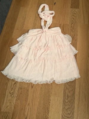 Ljusrosa volangklänning med knyt - Söt ljusrosa kortklänning med flera volanger och knyt i halsen. Klänningen har plisserat tyg och är ärmlös, perfekt för varma dagar. Materialet känns lätt och luftigt, vilket ger en romantisk och somrig känsla. Den är helt ny med pris lapp på💞