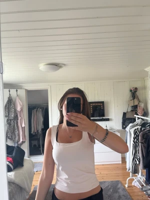 Vit linnetopp från Gina Tricot - Säljer en enkel och fräsch vit linnetopp från Gina Tricot. Toppen har breda axelband och en rak, något croppad passform. Perfekt till jeans eller kjol för en clean look. Materialet är mjukt och stretchigt, vilket gör den superbekväm.