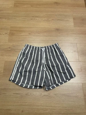 Randiga badbyxor från Zara - Snygga badbyxor från Zara i grått med vita vertikala ränder. De har elastisk midja med dragsko och innerbyxa i mesh för extra komfort. Perfekta för stranden eller poolen och ger en stilren look.