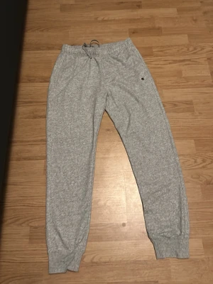 Gråa mjukisbyxor med dragsko - Snygga grå mjukisbyxor med resår i midjan och dragsko för skön passform. Byxorna har ribbade muddar vid bensluten och sidofickor. Perfekta för chill dagar hemma eller när du vill vara bekväm. Klassisk modell i mjukt material.