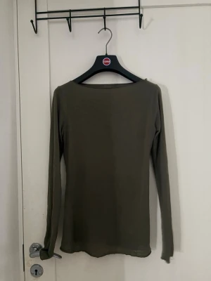 Olivgrön långärmad topp - En enkel och stilren olivgrön långärmad topp med rund halsringning. Toppen har en smal passform och är tillverkad i ett mjukt, stretchigt material som känns skönt mot huden. Perfekt att matcha med jeans eller kjol för en clean look.