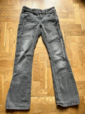 Grå bootcut jeans med broderade fickor - Säljer ett par grå bootcut jeans med snygga broderade bakfickor och knappar. Jeansen har klassisk femficksmodell och är tillverkade i denim med lätt tvättad look. 