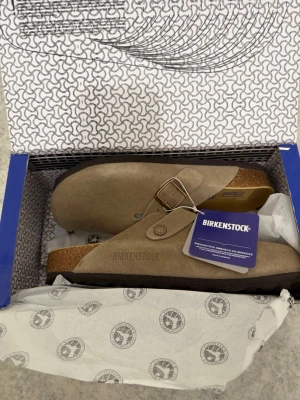 Beige Birkenstock tofflor mocka - Säljer ett par snygga beigea Birkenstock tofflor i mocka med klassisk korksula och justerbart spänne i metall. Modellen har en stilren design och är riktigt sköna att ha på sig. Perfekta för dig som gillar en avslappnad och trendig stil. ‼️Skickar inom 24H‼️ **PRIS KAN DISKUTERAS**