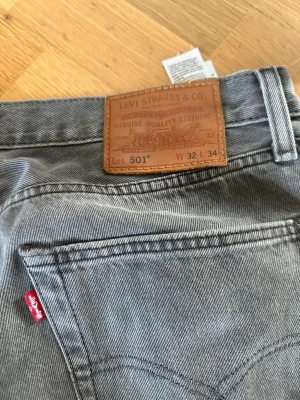 Grå Levi's 501 jeans - Säljer ett par klassiska grå Levi's 501 jeans med rak passform. Jeansen har den ikoniska läderlappen bak i midjan och röd Levi's-tagg på bakfickan. Tillverkade i slitstark denim, perfekta för en avslappnad och tidlös stil. 