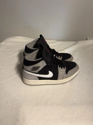 Svarta och grå jordans med mönster - Snygga jordans  i svart och grått med vit sula och vit swoosh på sidan. Skorna har ett unikt mönster på tåpartiet och klassisk hög siluett. Materialet är en mix av mocka och textil, och de har svarta skosnören.
