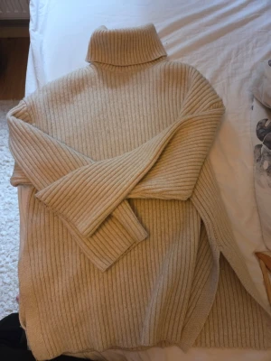 Beige ribbad polotröja - Säljer en beige stickad polotröja med ribbad struktur. Tröjan har lång ärm, hög krage och en loose passform som ger en avslappnad look. Perfekt för kyliga dagar och enkel att styla med jeans eller kjol.