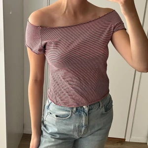 Randig topp röd/vit/blå - Säljer en croppad offshoulder topp med smala röda, blåa och vita ränder. Toppen har korta ärmar och är figurnära i modellen.