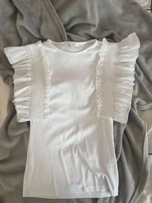 Vit blus med volangärmar - Supersöt vit blus med korta volangärmar och smockdetaljer. Storlek xs och i super bra skick💞