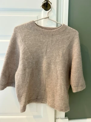 Beige stickad tröja med trekvartsärm - Mysig beige stickad tröja med rund halsringning och trekvartsärmar. Tröjan har en avslappnad passform och är tillverkad i ett mjukt material som känns skönt mot huden. Den är storlek S men skulle säga att den mer är XS. Materialet är alpacka och ull mm