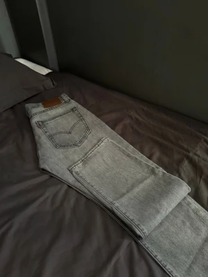 Grå raka jeans med fem fickor - Säljer ett par grå jeans med rak passform och klassisk femficksdesign. Jeansen har en ljus tvätt och är tillverkade i bomull. Perfekta för en avslappnad och stilren look.