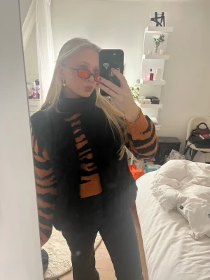 Tigermönstrad stickad tröja - Säljer en snygg stickad tröja med tigermönster i orange och svart. Tröjan har en croppad passform, långa ärmar och rund hals. Perfekt för dig som vill sticka ut med en trendig och djurinspirerad look.