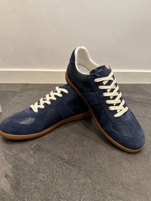 Mörkblå sneakers med mockadetaljer - Snygga mörkblå sneakers med ovandel i mocka och släta partier i läder. Skorna har vita snören, vit insida och klassisk gummisula i brunt. Perfekt för dig som gillar stilrena och tidlösa sneakers med en sportig touch.