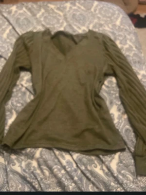 Olivgrön ribbad tröja med v-ringning - Snygg olivgrön tröja med v-ringning och långa, ribbade ärmar. Tröjan är gjord i ett mjukt, stretchigt material som känns skönt mot huden. Perfekt för dig som gillar stilrena basplagg med en twist.