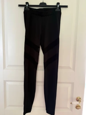Svarta leggings med meshdetaljer - Säljer ett par svarta leggings med snygga meshpaneler i diagonala ränder över låren. De har hög midja och är tillverkade i stretchigt material som sitter tight. Perfekta för dig som vill ha en sportig och trendig look. Kolla gärna mina andra annonser❗️