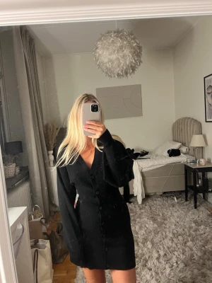 Svart stickad klänning med knappar - Snygg svart stickad klänning med långa ärmar och djup v-ringning, storlek 34. Från Gina Tricot 