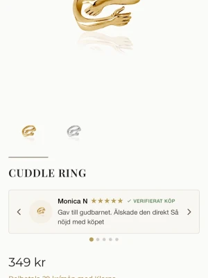 Guldfärgad Cuddle Ring - Unik ring i guldfärg med design av två armar som kramar om fingret. Ringen har en modern och stilren look som sticker ut och passar perfekt för dig som vill ha något annorlunda. Tillverkad i metall med blank finish.