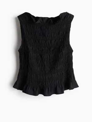 Svart smockad ärmlös topp - Snygg svart topp med smockad struktur och volangkant nertill. Ärmlös modell som ger en stilren och trendig look. Perfekt att matcha med jeans eller kjol för en cool outfit.
