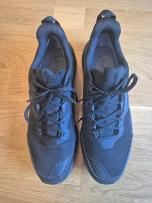 Svarta Adidas Terrex sneakers - Säljer ett par svarta Adidas Terrex sneakers med robust sula och meshdetaljer. Skorna har lågt skaft, snörning och diskret Terrex-logga på sidan. Perfekta för dig som gillar sportig och stilren look.