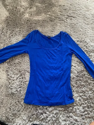 Kornblå långärmad topp - Säljer en kornblå långärmad topp med rund halsringning. Toppen har en slim passform och är tillverkad i ett mjukt, stretchigt material som sitter snyggt på kroppen. Perfekt att styla med jeans eller kjol för en enkel men snygg look.