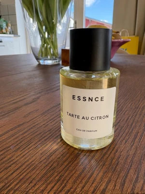 ESSNCE Tarte au Citron Eau de Parfum - Fräsch parfym från ESSNCE med doft av citronpaj. Flaskan är rund och genomskinlig med svart lock och enkel vit etikett. Perfekt för dig som gillar fräscha och söta citrusdofter.