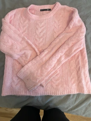 Ljusrosa kabelstickad tröja - Mysig ljusrosa kabelstickad tröja från H&M med rund halsringning och ribbade muddar. Tröjan har ett klassiskt flätmönster och är perfekt för att hålla värmen under kyliga dagar. Passar dig som gillar en söt och enkel stil.