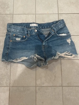 Lågmidjade  jeansshorts💗 - Säljer ett par blå jeansshorts från Gina, med slitna detaljer och fransig kant. Klassisk femficksmodell med knapp och dragkedja framtill. Perfekta till sommaren för en avslappnad och trendig look. Orginalpris: 400