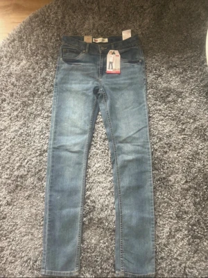 Levi's 510 Skinny Jeans blå denim - Säljer ett par Levi's 510 Skinny Jeans i klassisk blå denim. Jeansen har fem fickor, normal midja och smal passform hela vägen ner. Materialet är stretchigt för extra komfort och de har Levi's ikoniska läderpatch bak i midjan. Storlek 16 years old (176cm)