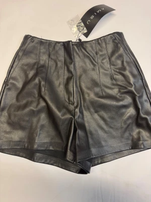 Svarta skinnshorts  - Snygga svarta shorts i skinnimitation från Amisu. De är högmidjade med stilrena sömdetaljer framtill och har en klassisk, rak passform. Oanvända. 
